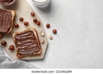Board of bread with chocolate paste and hazelnuts on white background, closeup