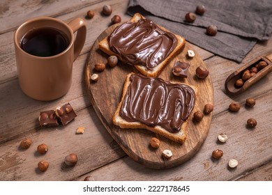 Board of bread with chocolate paste and hazelnuts on wooden background. Popular desser food. Top view.