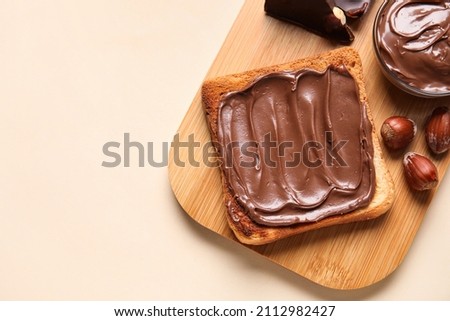 Board of bread with chocolate paste and hazelnuts on beige background, closeup