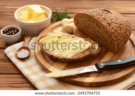 Board with fresh bread, different spices and bowl of butter on wooden background
