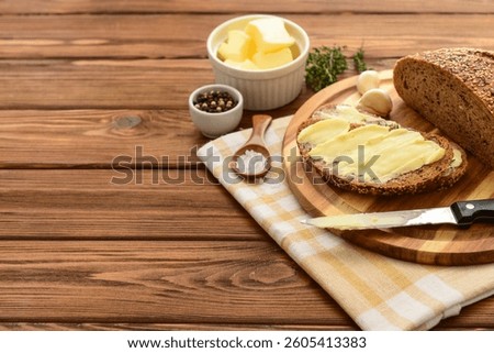 Board with fresh bread, different spices and bowl of butter on wooden background