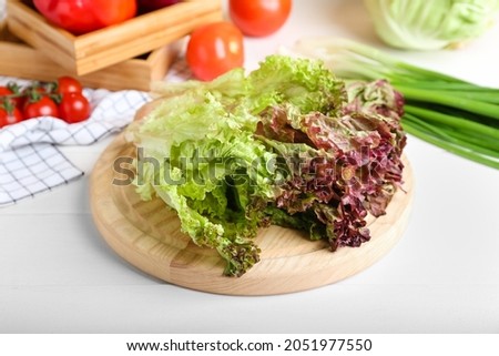 Board with fresh Lollo Rosso lettuce on white wooden background