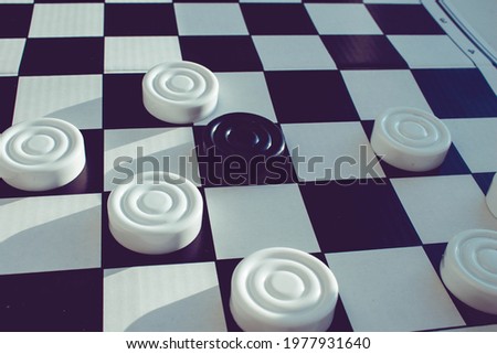 Board game of checkers. Black and white chips for the game. Chess field. Checkers move close-up. Checker in hand.
