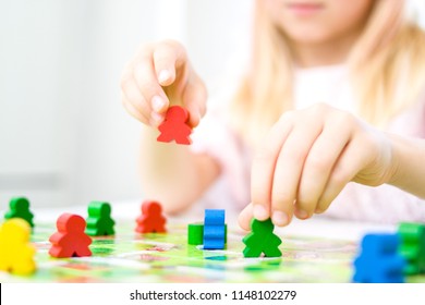 Board game and kids leisure concept - little blonde girl hold red people figure in hand. yellow, blue, green wood chips in children play