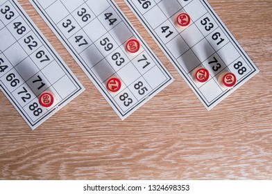 Board game lotto. Wooden lotto barrels and three game cards for a game in lotto on the top side of the picture. Wooden background. Group entertainment, family leisure. Vintage game. Top view. - Shutterstock ID 1324698353