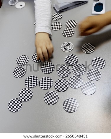 Board game, a visual perception exercise for visual therapy. Pieces of different colors and shapes are placed on the board according to rules. Children's hands playing a board game with pieces.