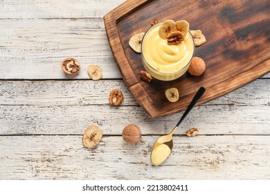 Board With Glass Bowl Of Vanilla Pudding, Walnuts And Banana Chips On Light Wooden Background