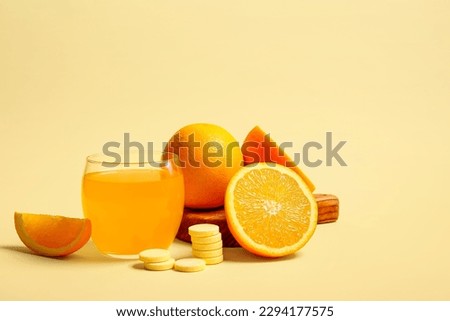 Board with glass of vitamin C effervescent tablet dissolved in water and oranges on beige background