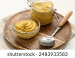 Board with jar of creamy mustard, spoon and bowl on white background, closeup