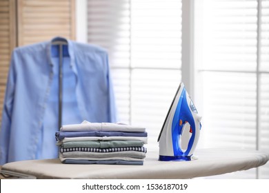 Board with modern iron and stack of clothes indoors, space for text. Laundry day