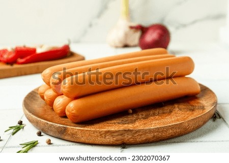 Board and plate of tasty sausages with tomatoes on white tile background