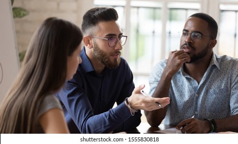 In Board Room Gathered Multi Racial Business People Focus On Serious Middle Eastern Ethnicity Team Leader Talking About Strategy, Corporate Goals, Share Ideas, Solve Problems Together At Group Meeting