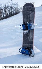 Board for snowboarding in the snow on the background of a ski slope, vertical photo. The concept of snowboarding, a winter sport