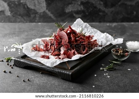 Board with spicy beef jerky on dark background
