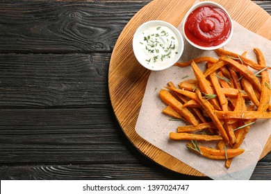 Board with sweet potato fries on wooden background, top view. Space for text