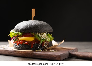 Board with tasty black vegetarian burger on table against dark background - Shutterstock ID 1311714524