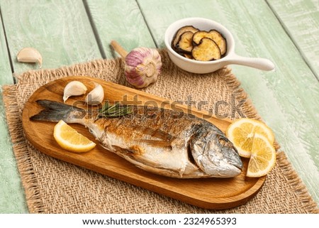Board with tasty grilled dorado fish on green wooden background