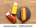 board with tasty hot dog, ketchup and mustard on wooden background