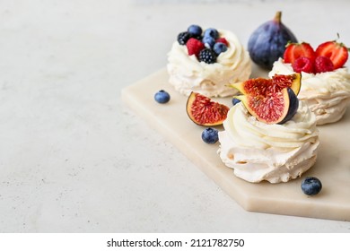 Board of tasty Pavlova cakes with berries on light background, closeup