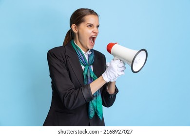 Boarding Announcement. Portrait Of Young Woman, Flight Attendant Shouting At Megaphone Isolated On Blue Studio Background. Model In Stewardess Uniform. Concept Of Business, Travel, Emotions