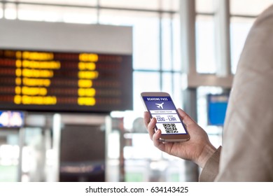 Boarding Pass In Smartphone. Woman Holding Phone In Airport With Mobile Ticket On Screen. Modern Travelling Technology And Easy Access To Aeroplane. Terminal And Timetable In The Blurred Background. 