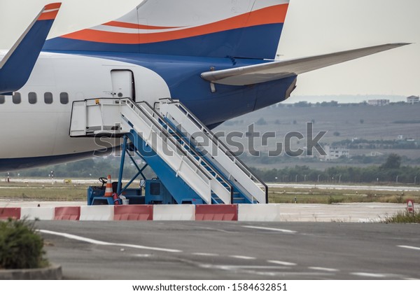 Boarding stairs ramp and back side of colorful\
airplane. Passenger stair car, aircraft steps next to door of\
commercial airliner on airport. Modern technology in fast\
transportation, business\
flights.
