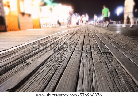 Boardwalk at night with glowing lights. People walking by carnival rides on the board walk in Ocean City, New Jersey.