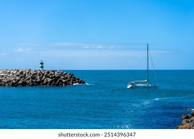 A boat approaches the entrance of Nazaré Marina, Portugal, with the lighthouse towers on both piers clearly visible, against a backdrop of calm waters and clear skies. - Powered by Shutterstock