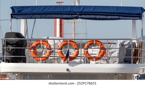 A boat with a blue canopy and orange life preservers on the railing. The boat is parked near a red and white sailboat - Powered by Shutterstock