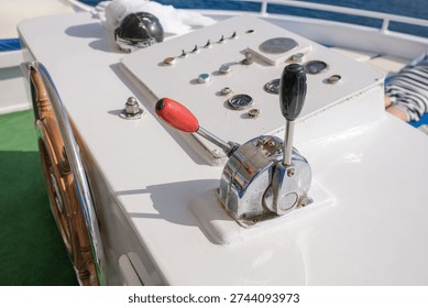 Boat control panel features a throttle lever and multiple gauges on a yacht deck, with clear blue water in the background