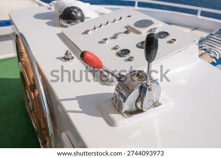 Boat control panel features a throttle lever and multiple gauges on a yacht deck, with clear blue water in the background