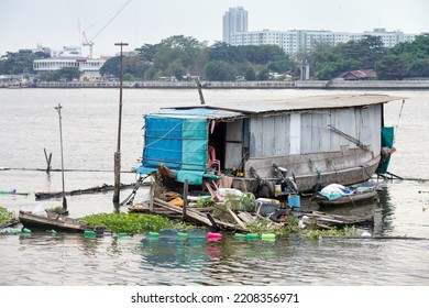 A Boat Converted Into A House Houseboats Moored In The Chao Phraya River. There Is A Blue Cloth To Protect From The Rain. A Red Chair There Are Plastic Bottles As Buoyancy And Cannabis Plants Are Plan