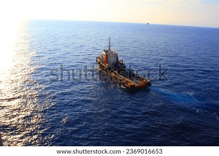 A BOAT CREW OR PRODUCTION SUPPORT VESSEL IS CURRENTLY IN THE SEA OF THE OFFSHORE OIL AND GAS DRILLING AREA. PHOTO WITH AERIAL DRONE VIEW