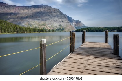 A Boat Dock And Fishing Pier Stretches Into The Calm Waters Of Swiftcurrent Lake At Glacier National Park In Autumn