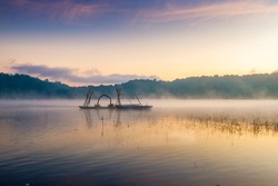 A Boat Floats In The Lake On A Foggy Misty Morning Surrounded By Mountains