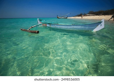 A boat floats on the clear, turquoise waters of Gili Labak, surrounded by pristine white sandy beaches and lush greenery, creating a serene and picturesque scene. - Powered by Shutterstock