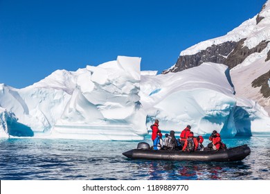 Boat full of tourists explore huge icebergs drifting in the bay near Cuverville island, Antarctic peninsula