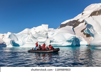 Boat full of tourists explore huge icebergs drifting in the bay near Cuverville island, Antarctic peninsula