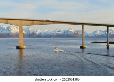 Boat at the Hadsel bridge, behind the snow-capped peaks of Hinnøya island, Langøysund in Stokmarknes, Nordland, Vesteralen, Norway