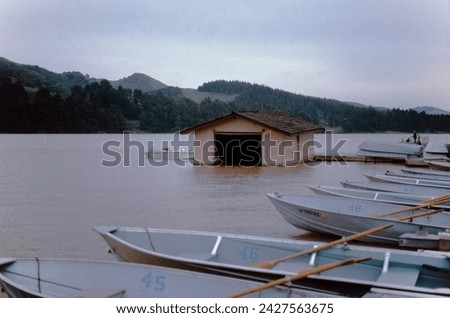 A boat house for rowboats sits on a mountain lake in Northern California on an overcast day. Rowboats and oars are in the foreground.