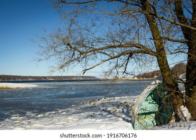 Boat leaning on tree in snow by water