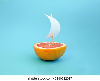 Boat made of grapefruit slice and paper sail against bright blue background. Original grapefruit decoration. Creative summer idea. Minimal style. Fruit concept.