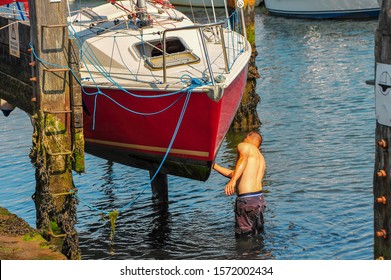 Boat Maintenance - Man cleans underside of boat in dry dock whilst standing in the water