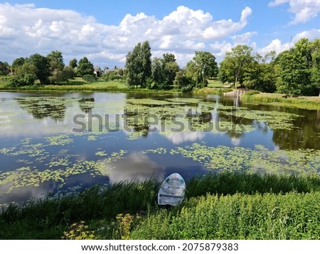 Boat near the shore of small lake among green trees on sunny summer day.
