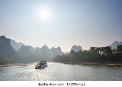 Boat on Li river cruise against the sun and karst formation mountain landscape in the fog between Guiling and Yangshuo, Guangxi province, China