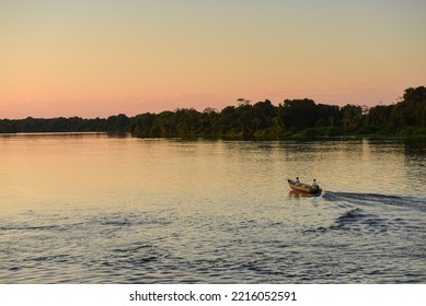 A Boat On The Rainforest-lined Guaporé-Itenez River At Sunset, Near The Remote Village Of Remanso, Beni Department, Bolivia, On The Border With Rondonia, Brazil