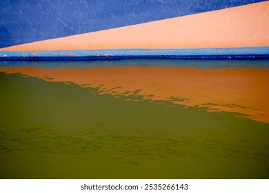 A boat painted in blue and light orange color is floating on a lake. The water surface mirrors the orange triangular shape. - Powered by Shutterstock