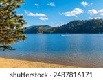 A boat passes in front of a small sandy beach at Beacon Point, a stop on the Centennial Trail, on lake Coeur d