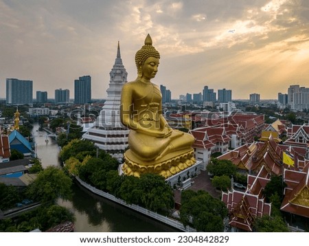 A boat was passing Big Buddha statue (Phra Buddha Dhammakaya Thepmongkhon ) in Wat Pak Nam Phasi Charoen temple located by the river during sunset.