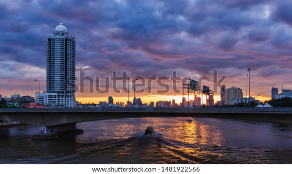 A boat is passing a bridge with a car running\
on a river in Bangkok,\
Thailand.
